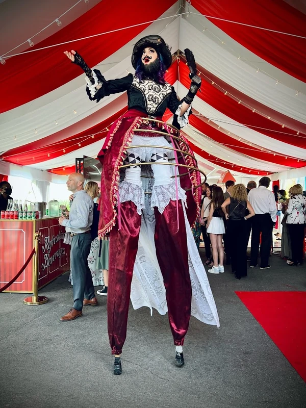 Victorian circus bearded lady stilt-walker in red velvet at corporate tent event
